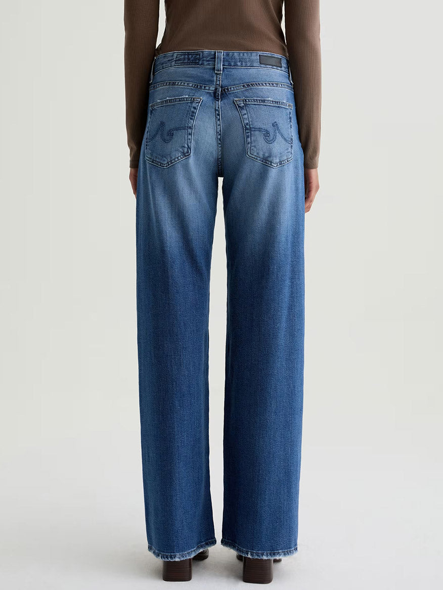 Person wearing AG Jeans Adria Low-Rise Wide Leg in Headline, premium Japanese denim, with a long-sleeve brown top, shown from the back against a plain background.