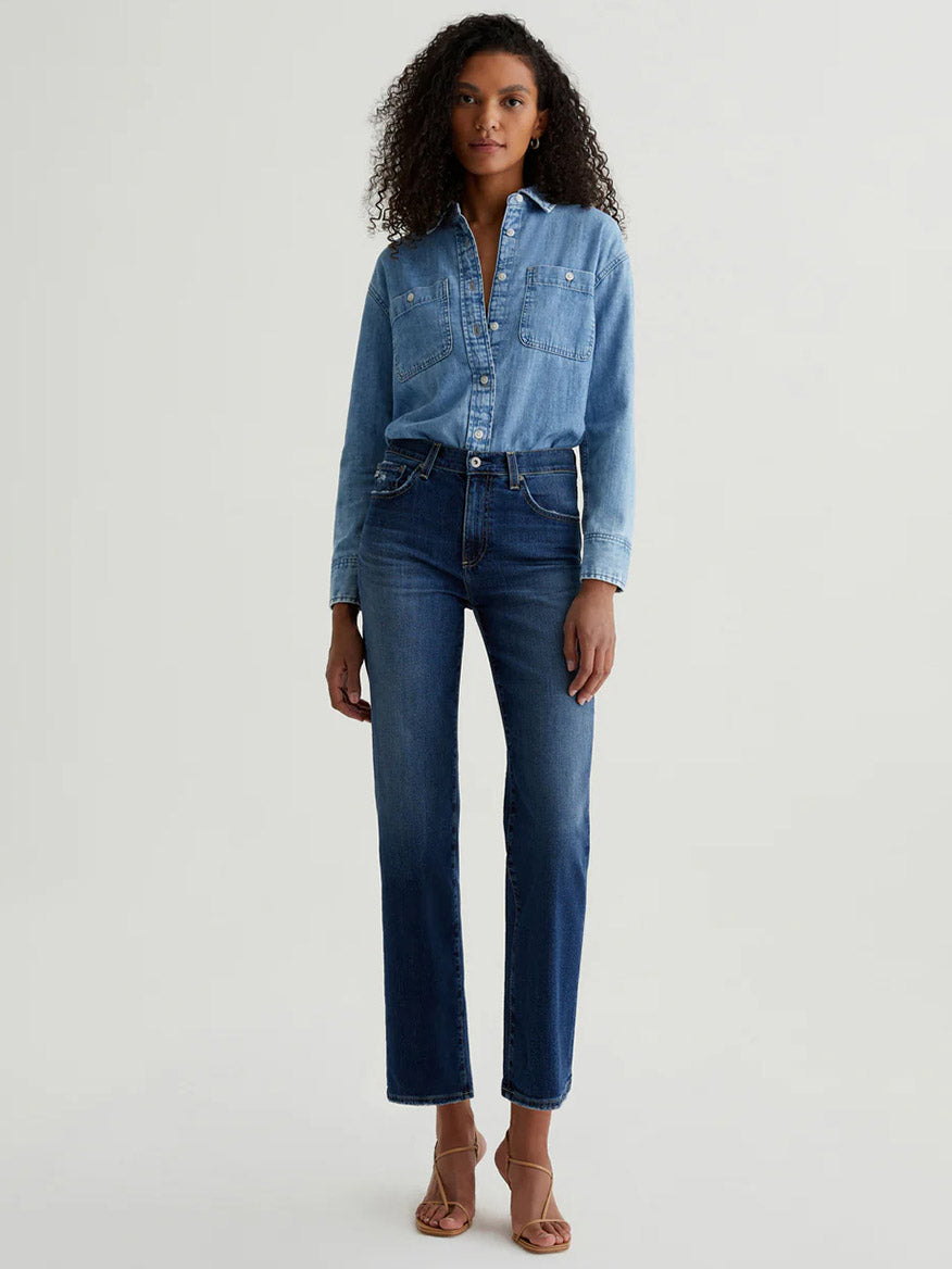 A person faces forward, wearing a light blue denim shirt, tan heeled sandals, and AG Jeans Brinley Crop in 7 Years La Jolla against a plain light background.