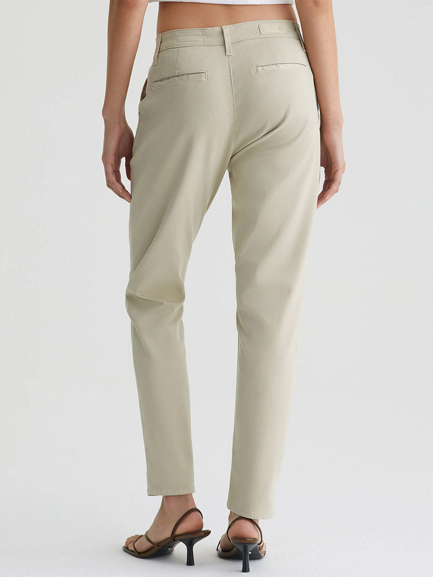 A person wearing AG Jeans Caden in Cream Froth tailored trousers for women and black heels standing with their back to the camera.