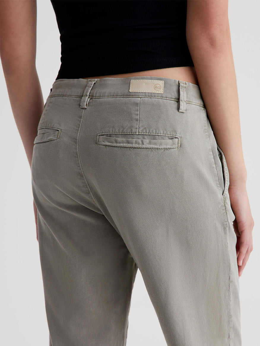 Close-up view of a person wearing light-colored AG Jeans Caden in Dried Parsley chino pants with a black top, focusing on the chino pants' back pocket and waistband.