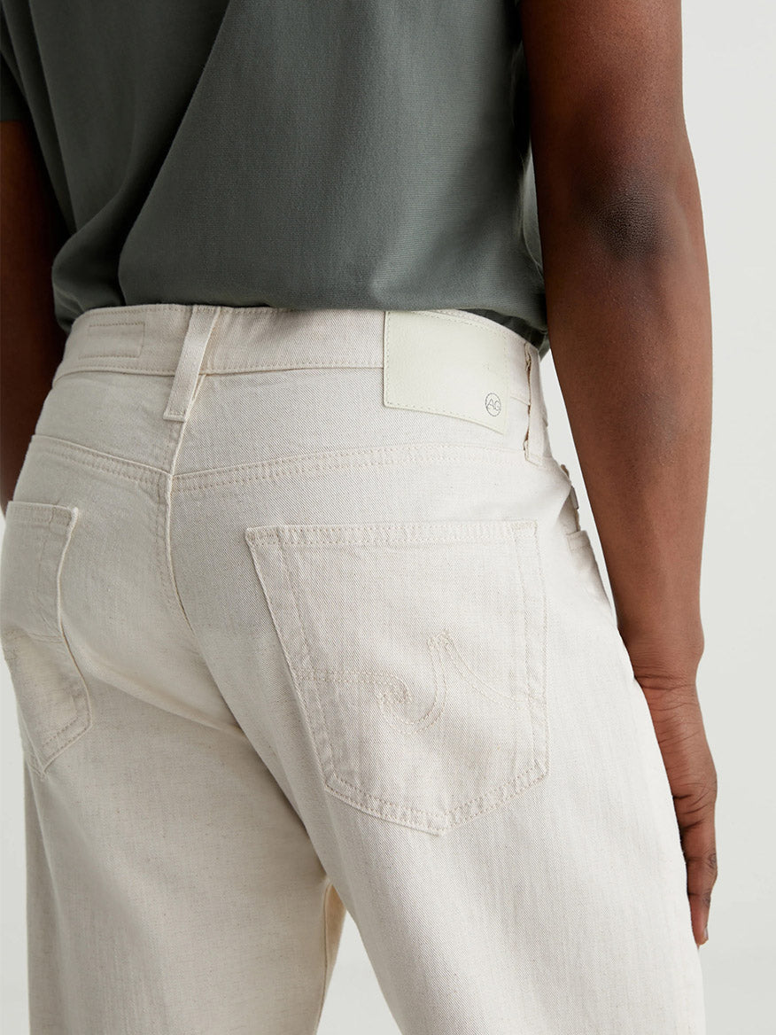 Person wearing a grey shirt and AG Jeans Everett in Natural, shown from the waist down and back. The off-white slim straight jeans feature a mid-rise waist, two rear pockets, and a light patch above the right rear pocket.