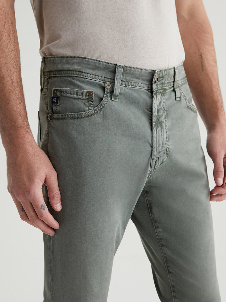 Man standing to showcase a pair of AG Jeans Everett Sueded in Sulfur Thorn Field, with a focus on the front pocket area.