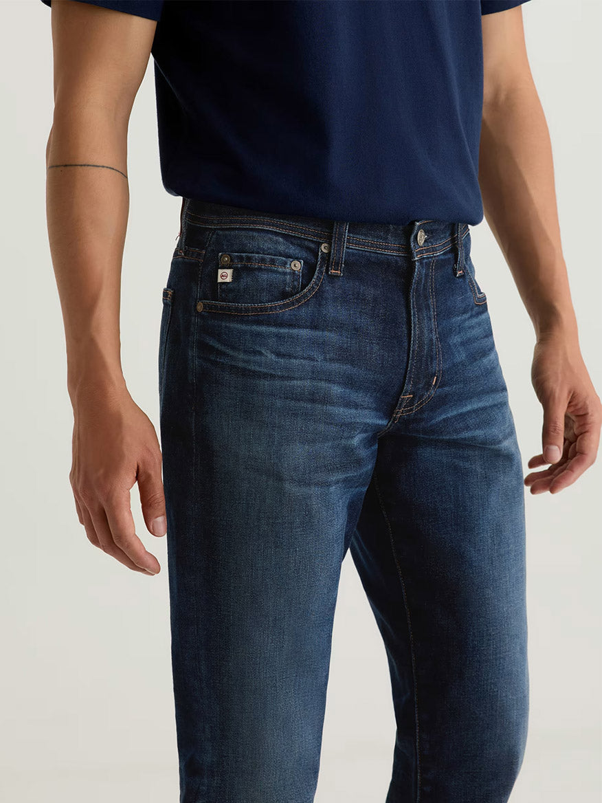 A person wearing the AG Jeans Graduate in 4 Years Martel, relaxed fit men's jeans made from comfort stretch denim, stands with arms relaxed by their sides.