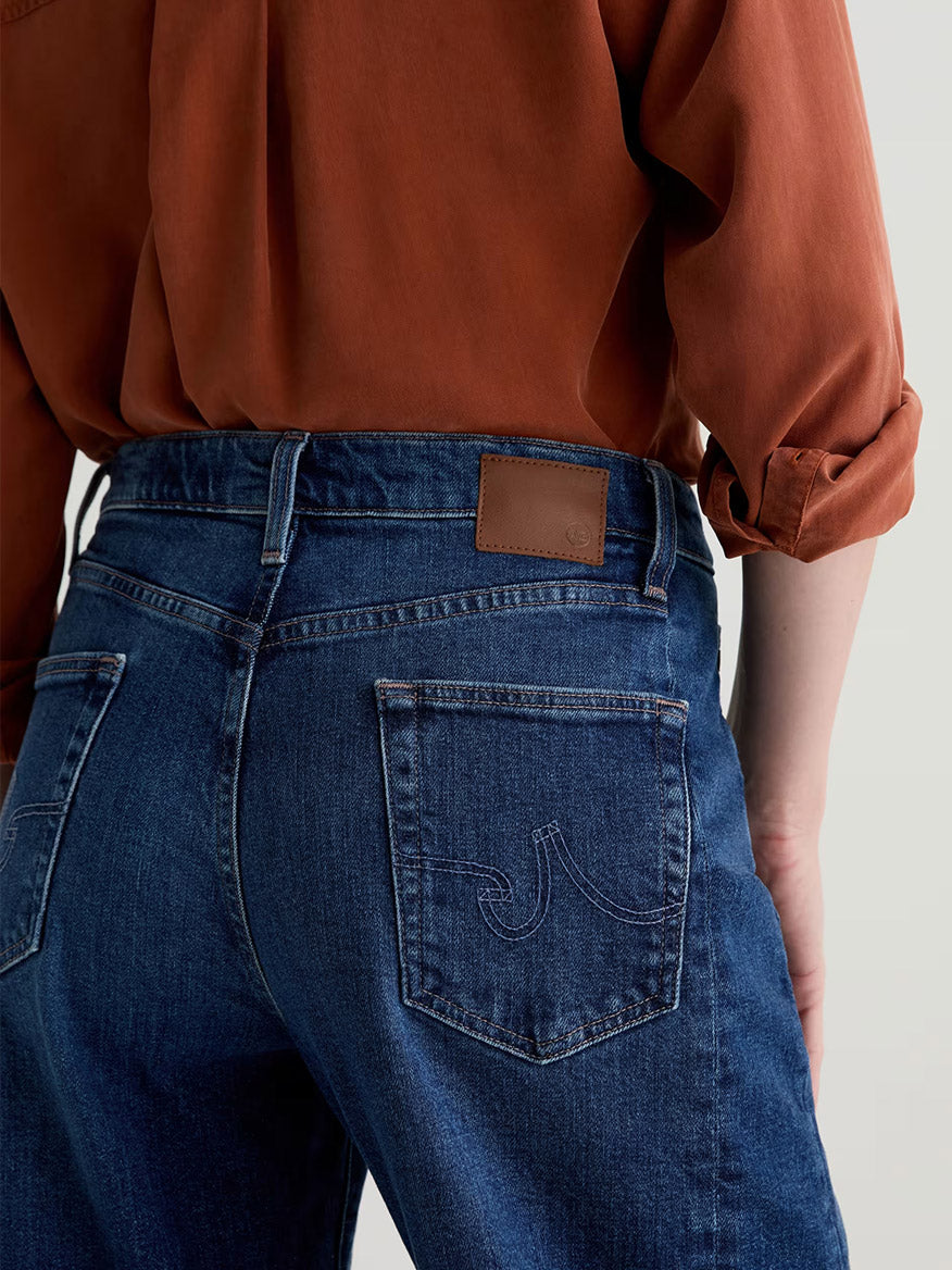 Person wearing AG Jeans Hattie High Rise Barrel in Vapor Wash Dynasty and a rust-colored shirt, shown from the back with hands by their sides.