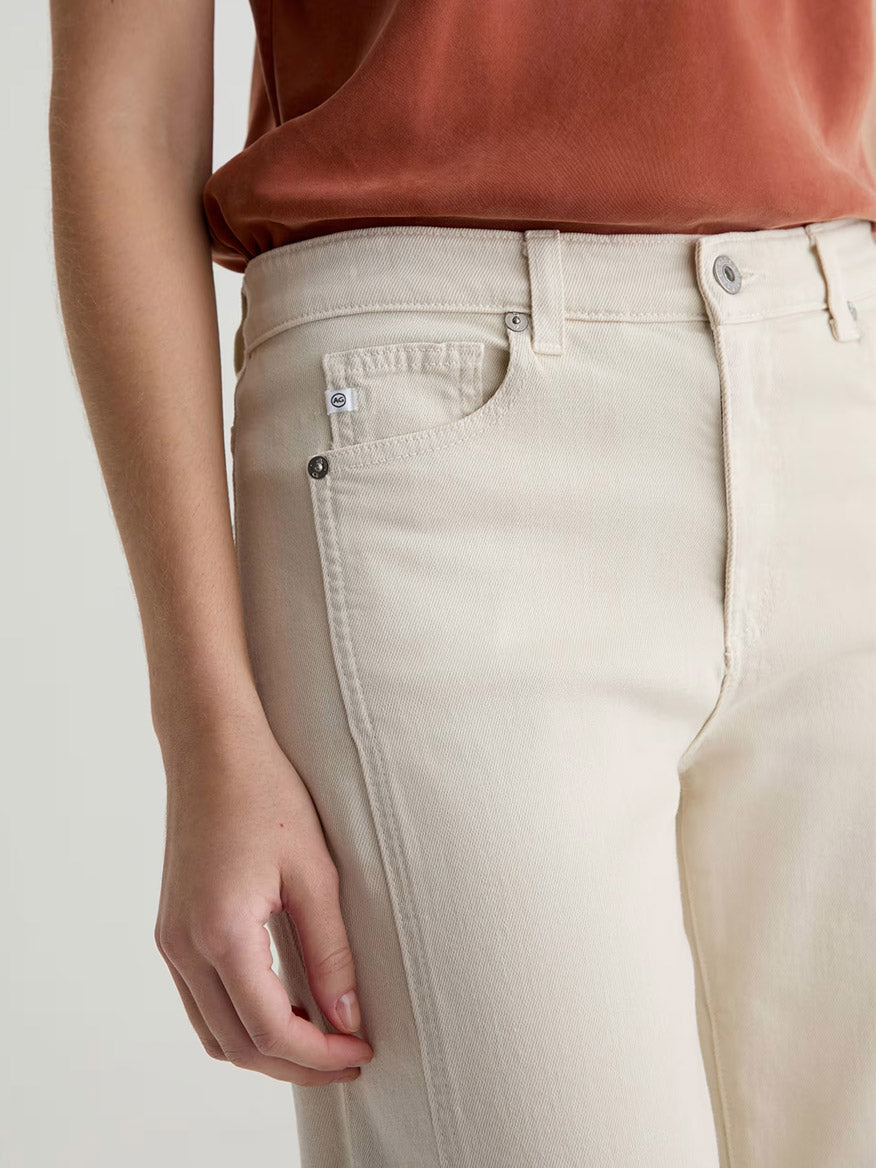 A person wearing a rust-colored top and AG Jeans Saige Wide Leg Crop With Panel in Opal Stone, with one hand relaxed by their side.