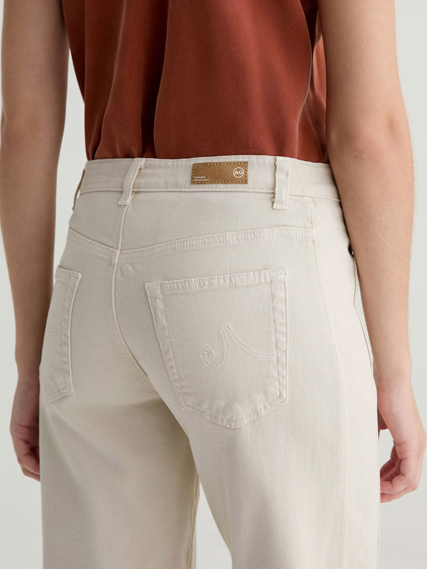 A person wearing a rust-colored shirt and AG Jeans Saige Wide Leg Crop With Panel in Opal Stone, shown from the back, featuring visible pockets and belt loops.