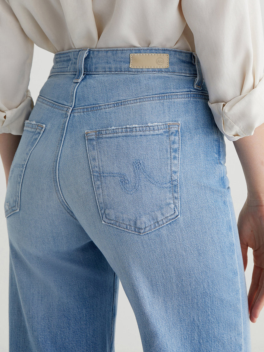 A person shown from the back wearing AG Jeans Saige Wide Leg Crop in Dana Point light blue jeans and a white long-sleeve shirt.