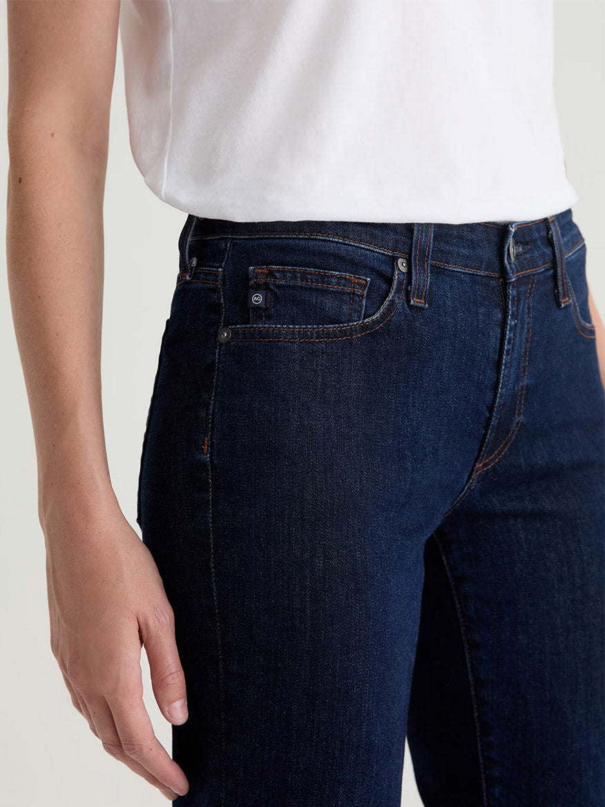 A person wearing a white t-shirt and AG Jeans Sandra Low-Rise Straight in Modern Indigo, shown from torso to mid-thigh, with their left arm relaxed at their side.