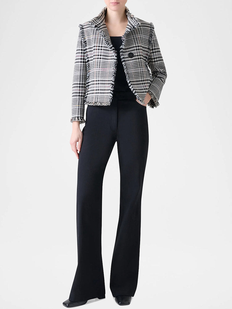 A person stands against a plain light background, wearing a black top, black flared pants, black shoes, and the Akris Punto Check Fringe Hem Cropped Jacket in Cream/Black.