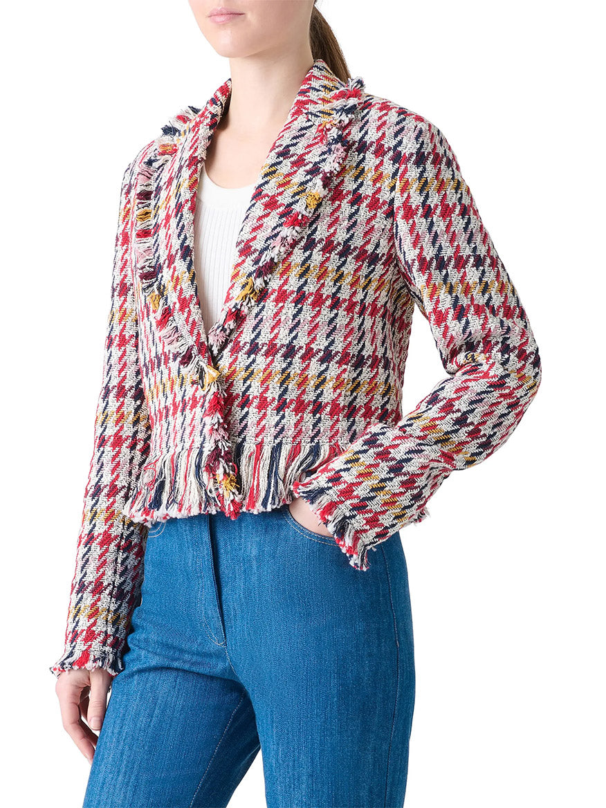 A person wearing the Akris Punto Houndstooth Tweed Fringe Trim Blazer in Cream Multi over a white top and blue jeans, shown from the waist up.