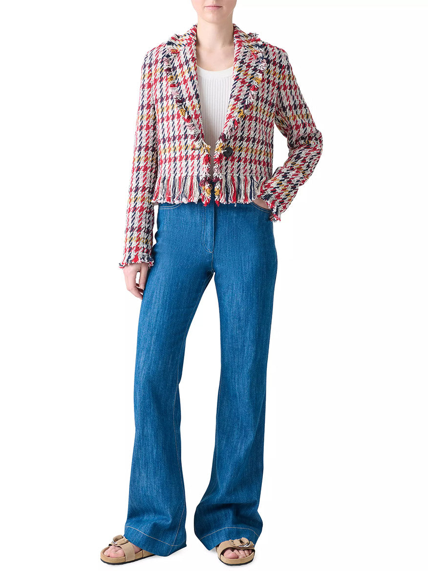 Person wearing the Akris Punto Houndstooth Tweed Fringe Trim Blazer in Cream Multi, paired with a white ribbed top, blue high-waisted flared jeans, and sandals, standing against a plain white background.