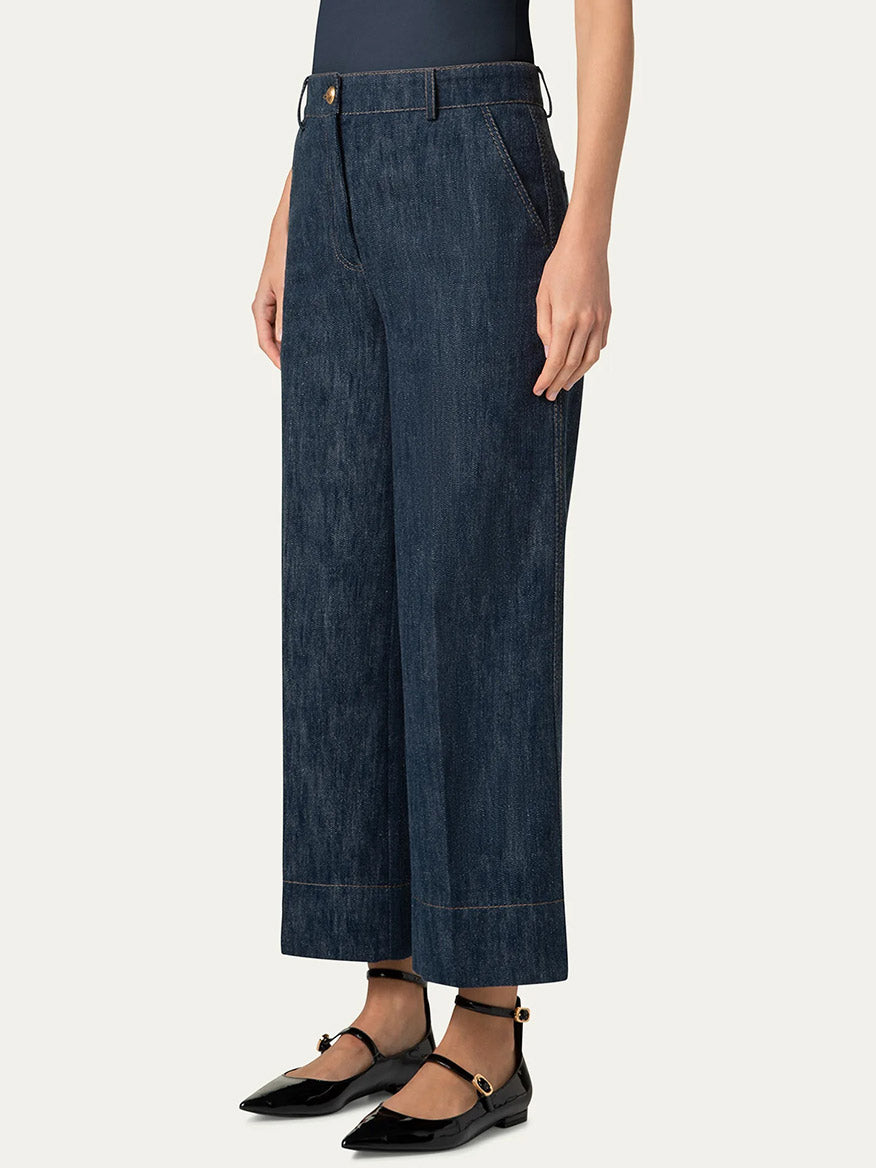 A person wearing Akris Punto Chiara Wide Leg Denim Jeans in Navy and black pointed flats with ankle straps stands against a plain backdrop.