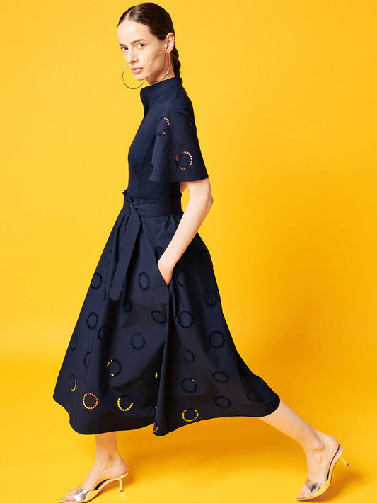 Woman in a Akris Punto Fit and Flare Midi Shirt Dress with Circle Eyelets in Navy, walking against a yellow background.