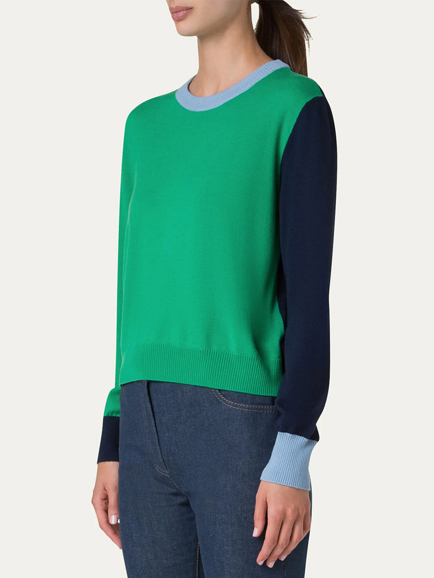 Person wearing an Akris Punto Colorblock Merino Sweater in Sea Green/Navy/Sky with relaxed fit and long sleeves, paired with dark jeans, shown from the side.