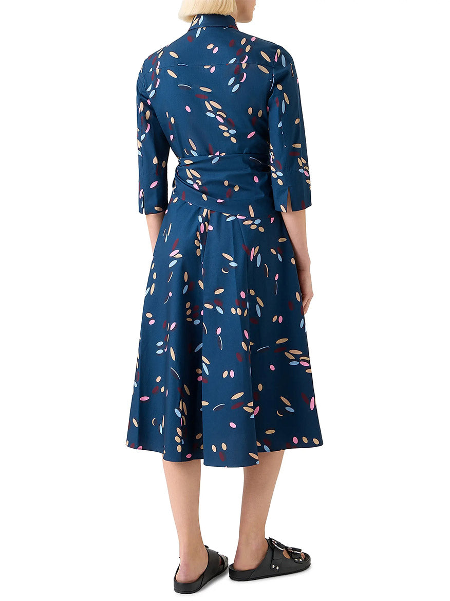 A woman stands with her back to the camera, wearing the Akris Punto Confetti Print Wrap Dress in Ink Multi and black flat shoes.
