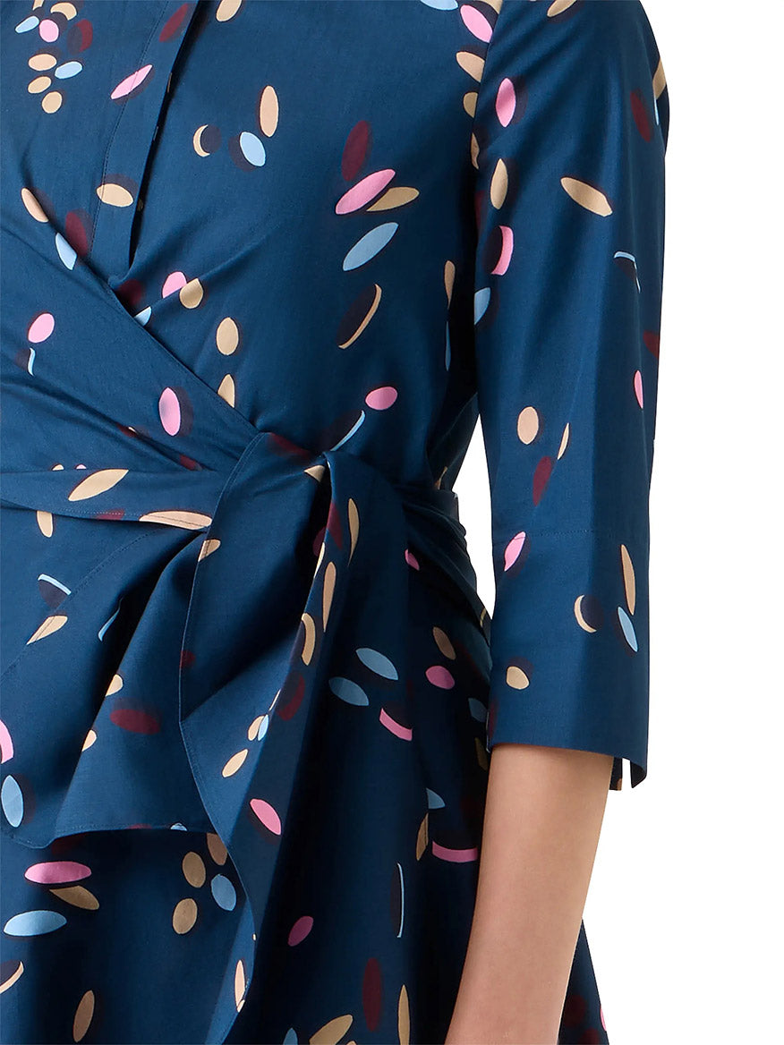 A person wears the Akris Punto Confetti Print Wrap Dress in Ink Multi, featuring a blue confetti print, three-quarter sleeves, and a tied waist belt.