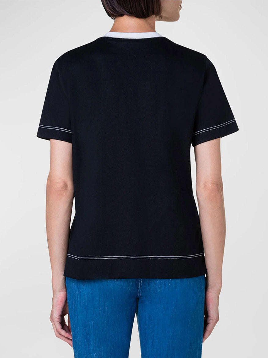 The back view of a woman wearing an Akris Punto Contrast Stitching Trim T-Shirt in Black and jeans.