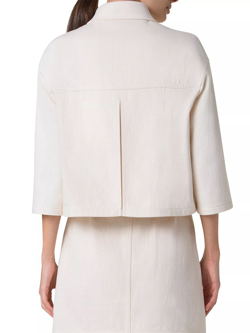 A person is seen from behind wearing the Akris Punto Asymmetrical Cotton Blend Biker Jacket in Cashew, a light-colored, three-quarter sleeve jacket with a center seam and an asymmetric snap closure. It pairs seamlessly with a skirt for a modern twist.