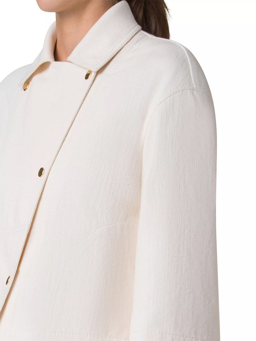 A person is shown from the shoulders down wearing an Akris Punto Asymmetrical Cotton Blend Biker Jacket in Cashew featuring a white, textured biker style with a high collar and gold buttons.