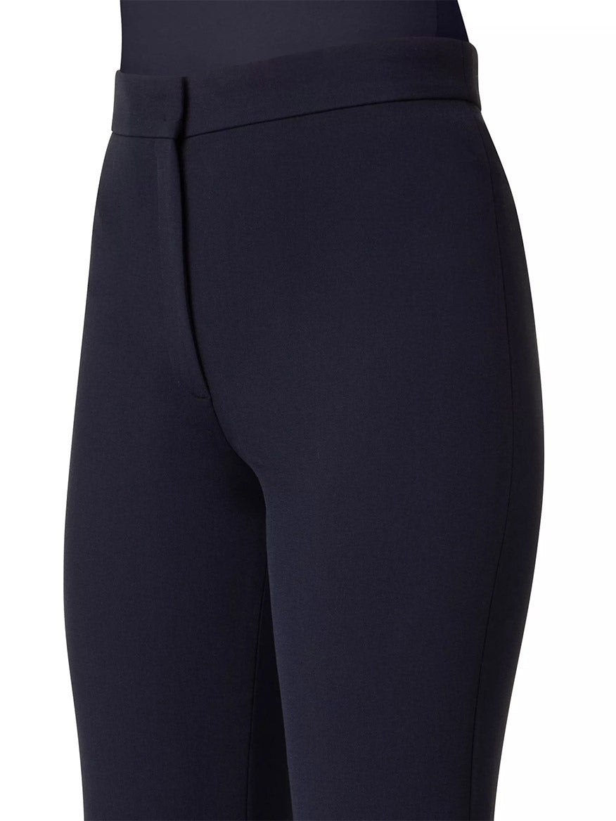 Close-up of someone wearing Akris Punto Courtney Crepe Boot-Cut Pants in Navy, featuring a waistband and front seam crafted from stretchy pebble crepe. The design offers a leg-lengthening effect against the plain background.