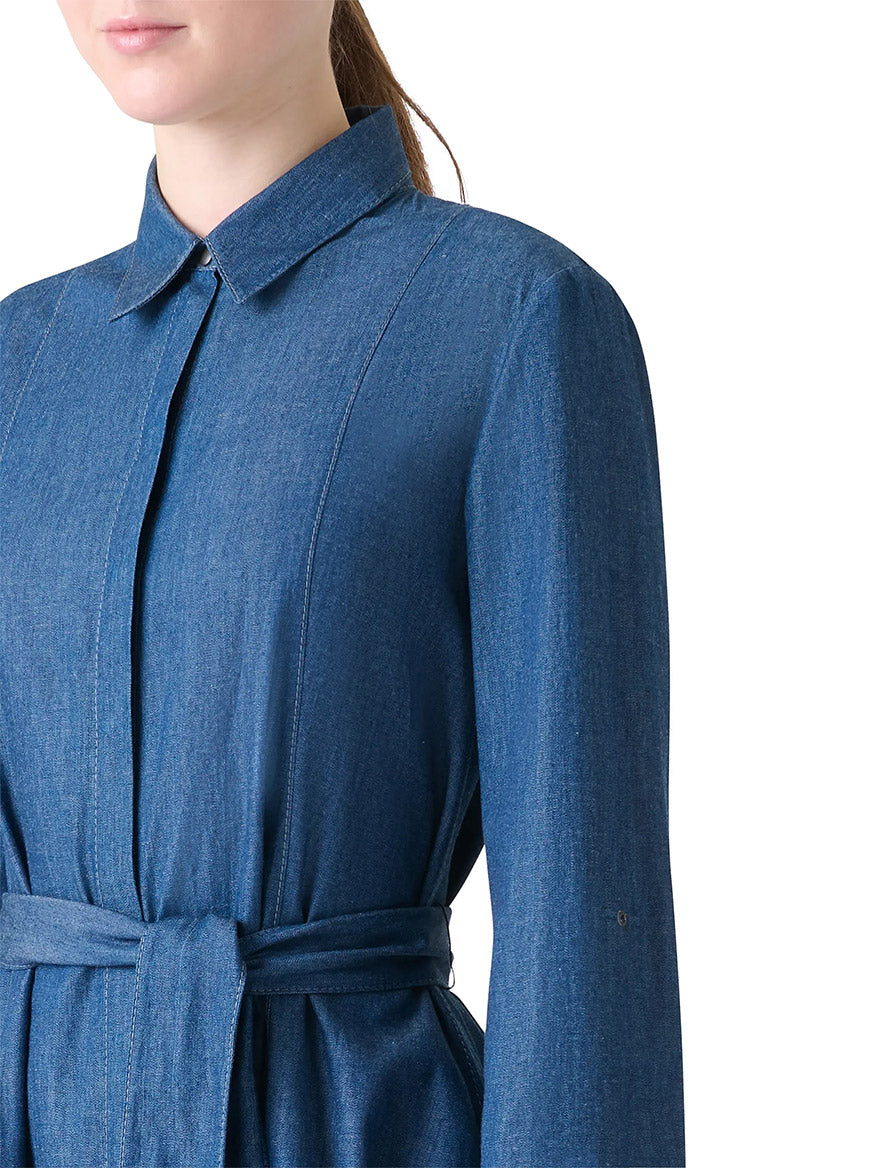 A model wears the Akris Punto Tie-Waist Denim Shirtdress in Medium Blue, featuring bracelet-length sleeves and a matching waist tie, shown from shoulders to mid-waist against a white background.