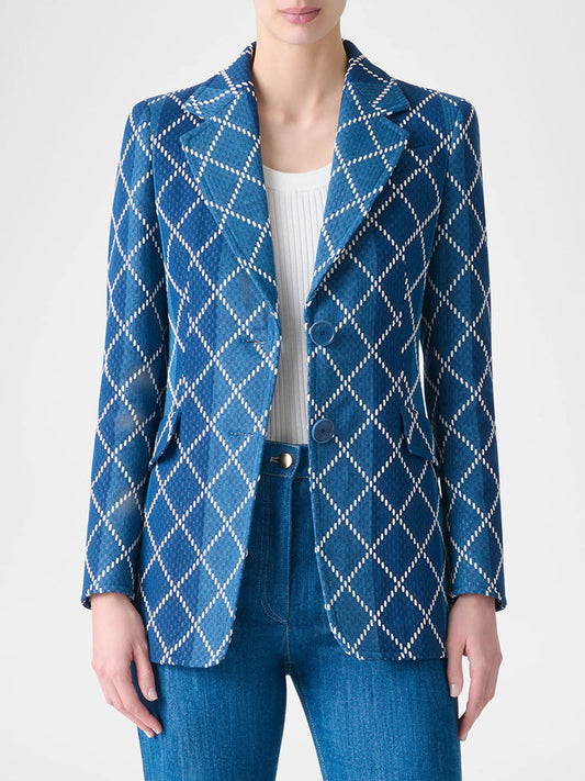 Wearing the Akris Punto Diamond Cotton Jacquard Fitted Blazer in Medium Blue Multi over a white top and blue jeans, a person stands against a plain background.