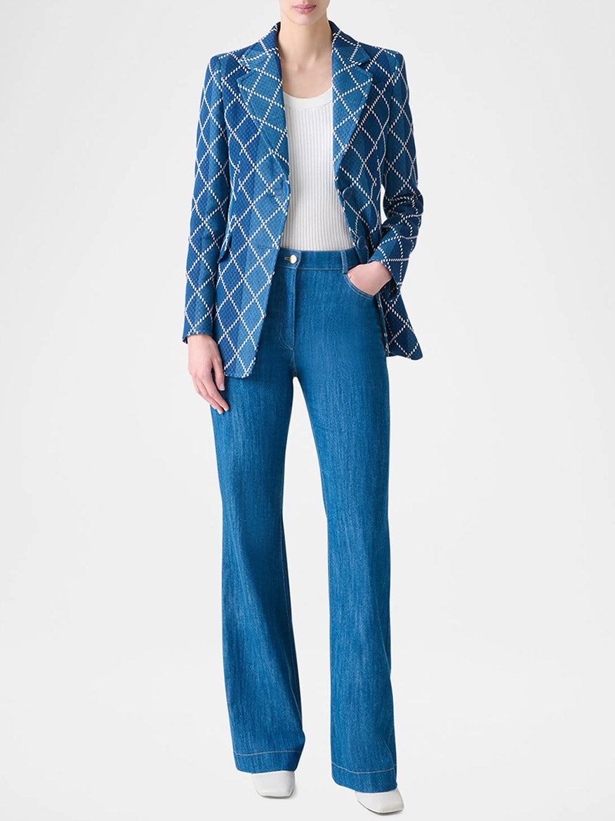 Person in an Akris Punto Diamond Cotton Jacquard Fitted Blazer in Medium Blue Multi, white ribbed top, and high-waisted blue jeans, standing against a plain light background.
