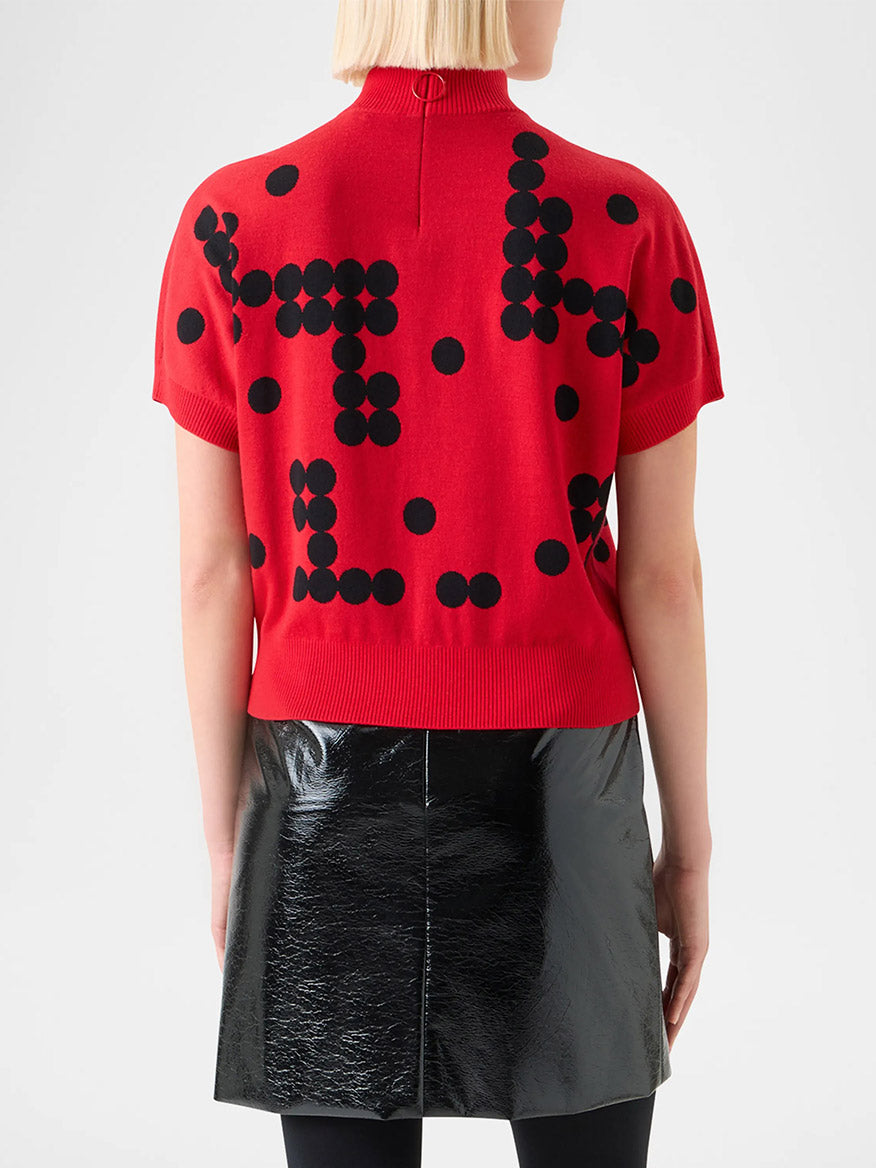 Someone shown from the back wears the Akris Punto Dot Grid Jacquard Knit Sweater in Vermillion/Black with a black shiny skirt.