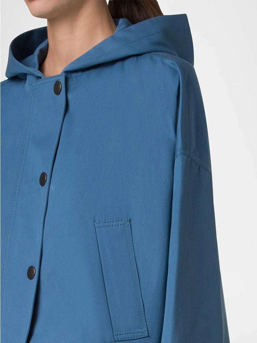 A close-up of a person wearing the Akris Punto Cotton Gabardine Carcoat in medium blue with black snap buttons and a front pocket, shown from the shoulders down.