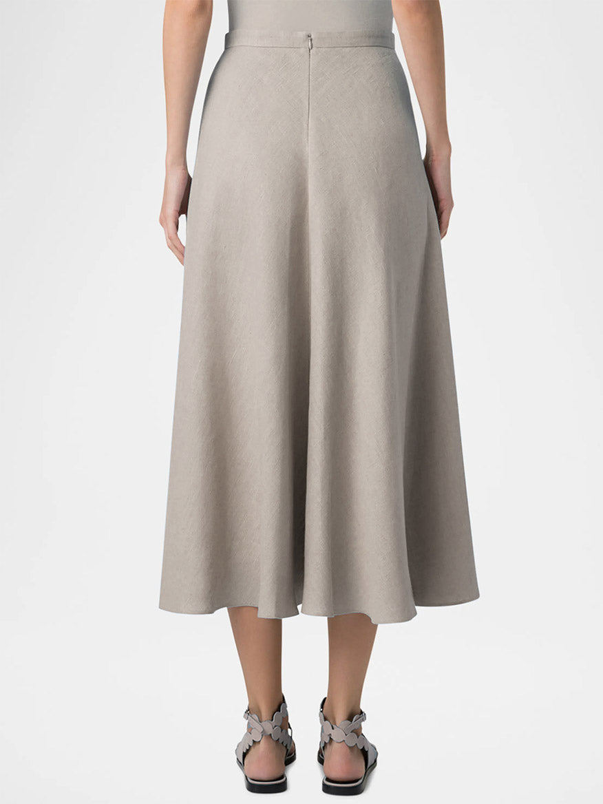 A person stands facing away, wearing the Akris Punto Raw Linen 3D Carnation Midi Skirt in Chalk paired with open-toe sandals featuring a 3D carnation floral design.