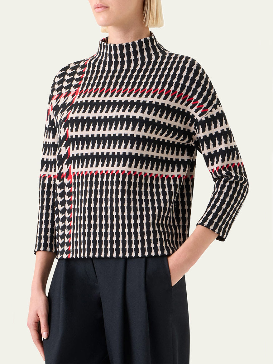 A woman wears the Akris Punto Mock Neck Plaid Sweater in Black/Cream/Vermillion with three-quarter sleeves and black pants, standing against a plain background.