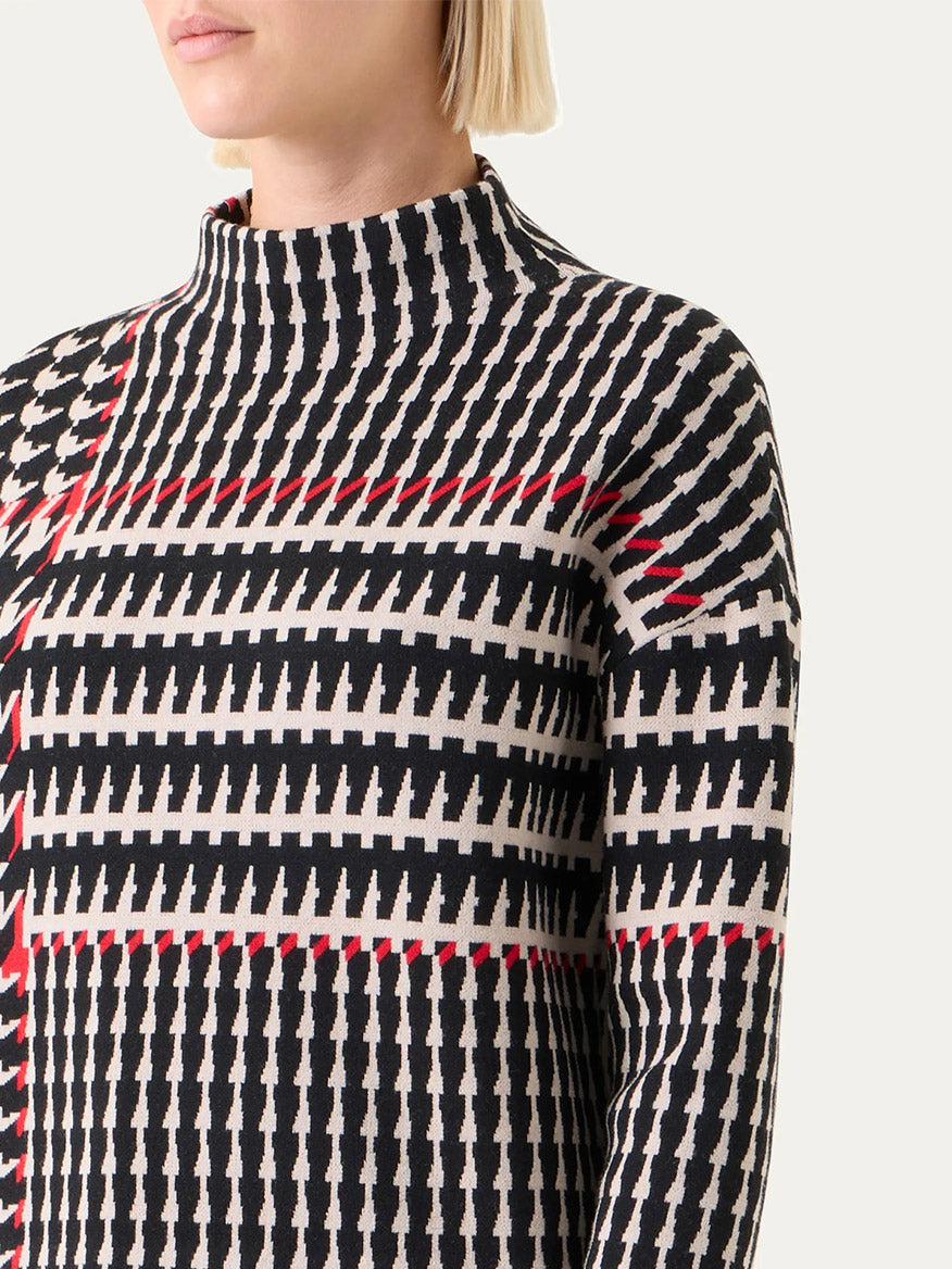 A person with short blonde hair wears the Akris Punto Mock Neck Plaid Sweater in Black/Cream/Vermillion, a high-neck, long-sleeve knit with a bold geometric pattern.