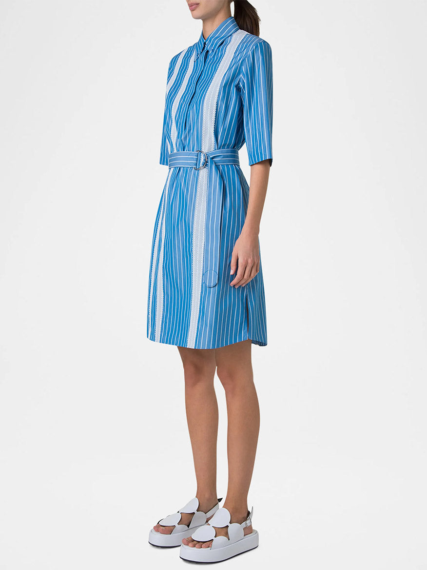 A woman wears the Akris Punto Pajama Stripe Collared Dress in Medium Blue/Cream with a D-ring self-belt, short sleeves, and white platform sandals.
