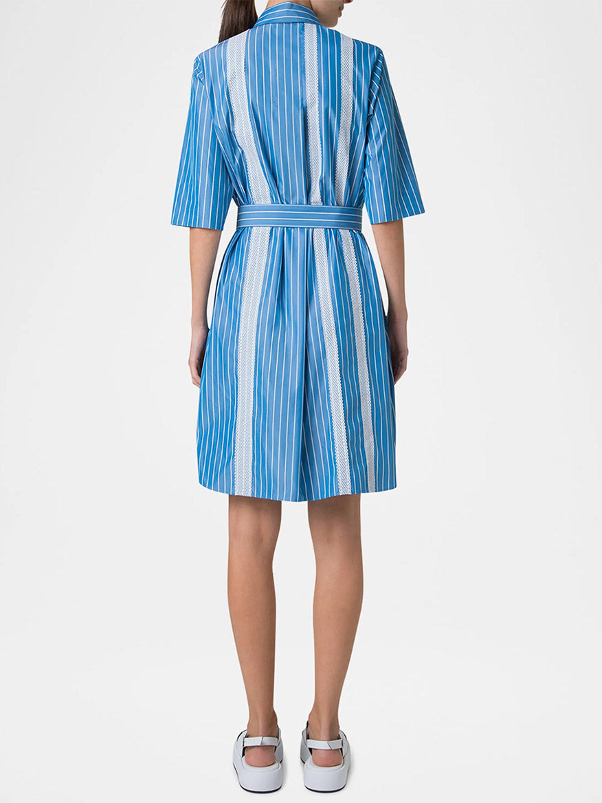 A woman faces away wearing the Akris Punto Pajama Stripe Collared Dress in medium blue/cream, featuring a D-ring self-belt and short sleeves, paired with white shoes.