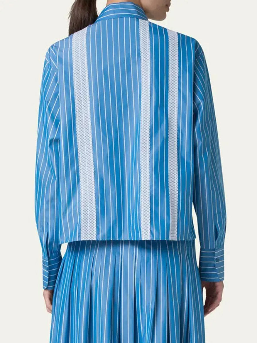 A person shown from the back wears the Akris Punto Pajama Stripe Boxy Collared Shirt in medium blue and cream, paired with a matching pleated skirt, set against a plain background.