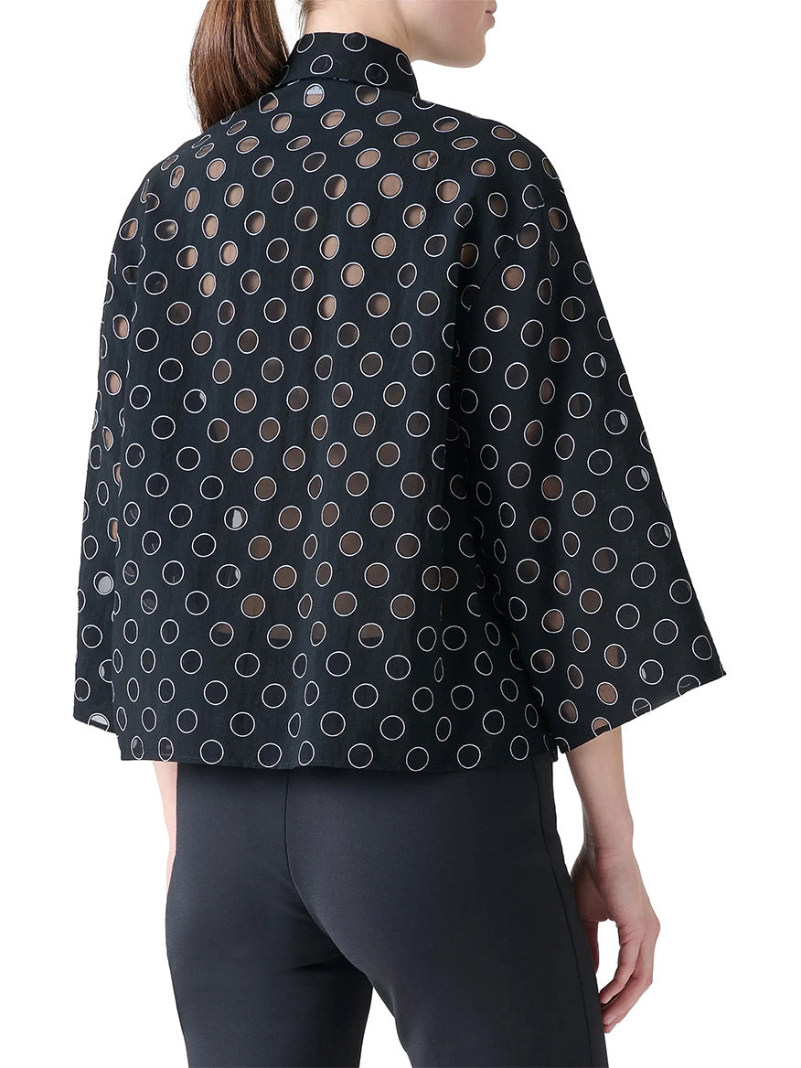 A person is seen from the back wearing the Akris Punto Boxy Polka Dot Organzino Blouse in Black/Cream over black pants, its loose fit and polka dot pattern creating a modern, standout look.