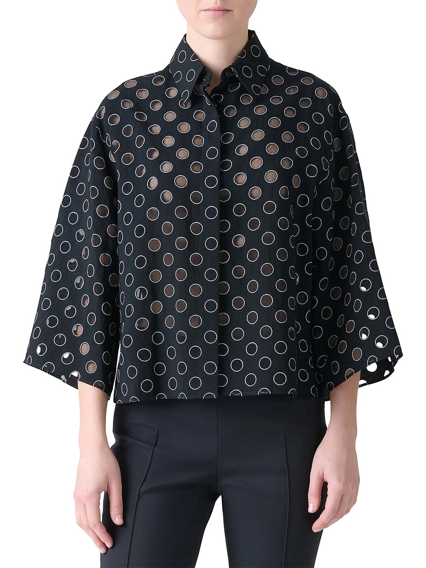A person wearing the Akris Punto Boxy Polka Dot Organzino Blouse in Black/Cream, featuring wide sleeves and circular cutouts, paired with black pants.