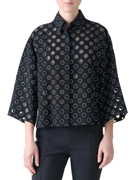 A person wearing the Akris Punto Boxy Polka Dot Organzino Blouse in Black/Cream, featuring wide sleeves and circular cutouts, paired with black pants.