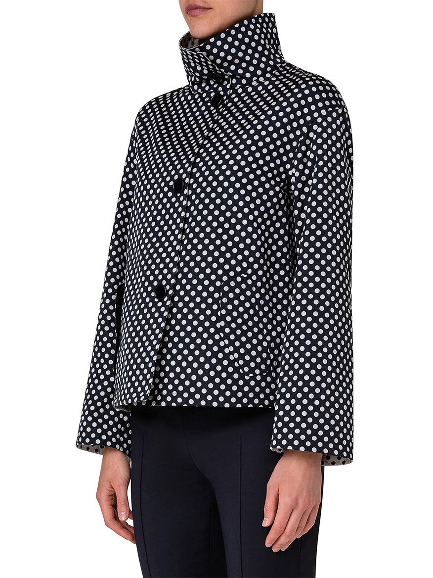 A person wearing the Akris Punto Reversible Polka Dot Jacket in Black/Cream with a high collar and dark pants stands against a plain background.