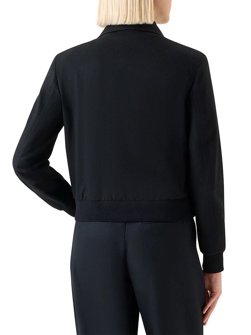 A person with short blonde hair is seen from the back wearing the Akris Punto Wool/Cashmere Short Bomber Jacket in Black and black pants, featuring rib-knit trim.