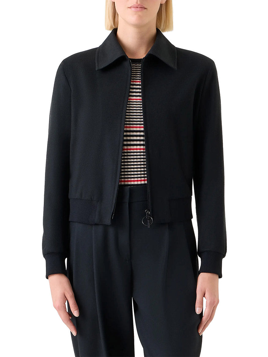 A person wears the Akris Punto Wool/Cashmere Short Bomber Jacket in Black over a striped shirt and black pants, standing with arms relaxed at their sides.