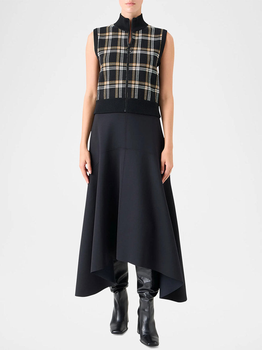 Someone wears the Akris Punto Sleeveless Plaid Jacquard Zip Sweater in Black/Cream/Camel over a black asymmetrical midi skirt and black knee-high boots, standing against a plain background.
