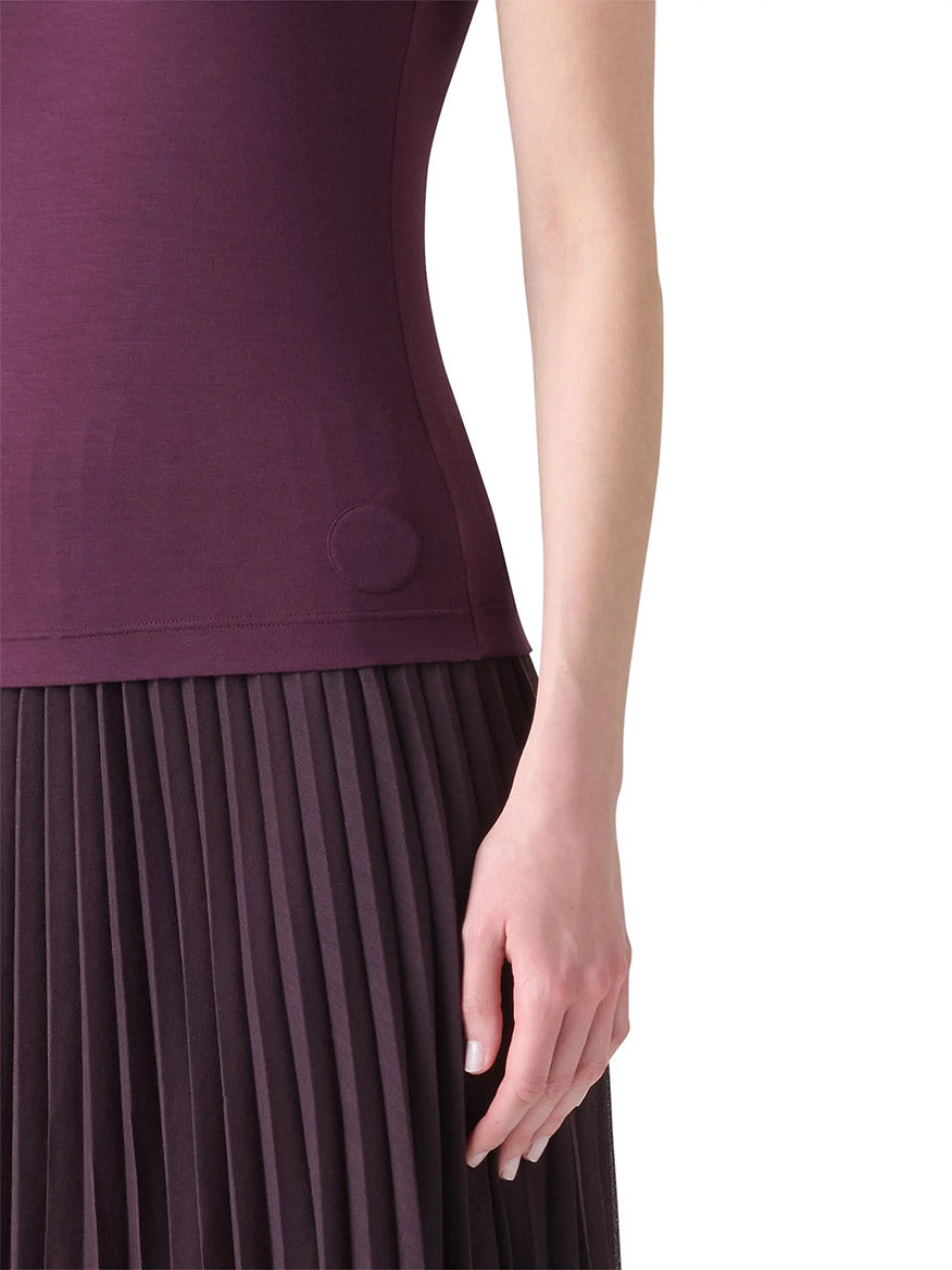 A person wearing a sleeveless, fitted Akris Punto Square-Neck Jersey Tank Top in Blackberry and a pleated dark purple skirt, shown from the shoulder to mid-thigh, with one arm relaxed at their side.