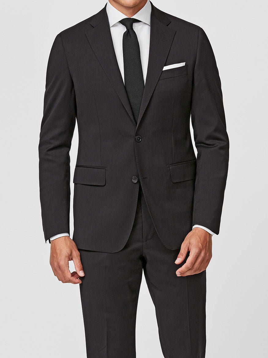 A man wearing the Atelier Munro Black Twill 4-Season Wool Stretch Suit with a white dress shirt, black tie, and white pocket square stands against a plain background.