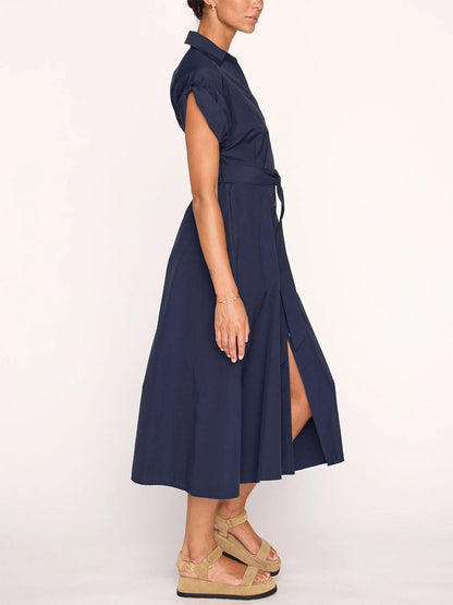 Side view of a woman wearing a Navy Brochu Walker Fia Belted Dress with a shirtdress silhouette, featuring a high slit tied at the waist, paired with beige platform sandals.