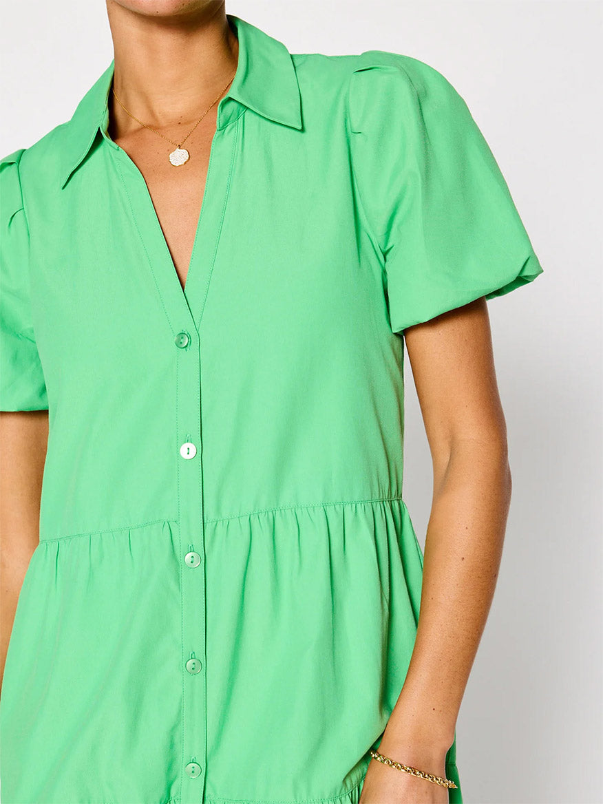 Close-up of a person wearing a bright green short-sleeved Brochu Walker Havana Dress in Derby Green with buttons and a collar, accessorized with a gold necklace and bracelet.