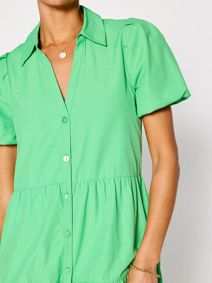 Close-up of a person wearing a bright green short-sleeved Brochu Walker Havana Dress in Derby Green with buttons and a collar, accessorized with a gold necklace and bracelet.