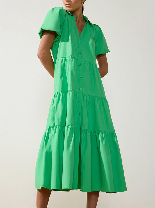 A woman in a bright green, knee-length Brochu Walker Havana Dress in Derby Green with short sleeves, a collared neckline, and tiered skirt.