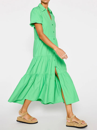 Woman in a flowing green midi Brochu Walker Havana Dress in Derby Green with tiered skirt and ruffle hem, paired with beige sandals, walking against a plain background.