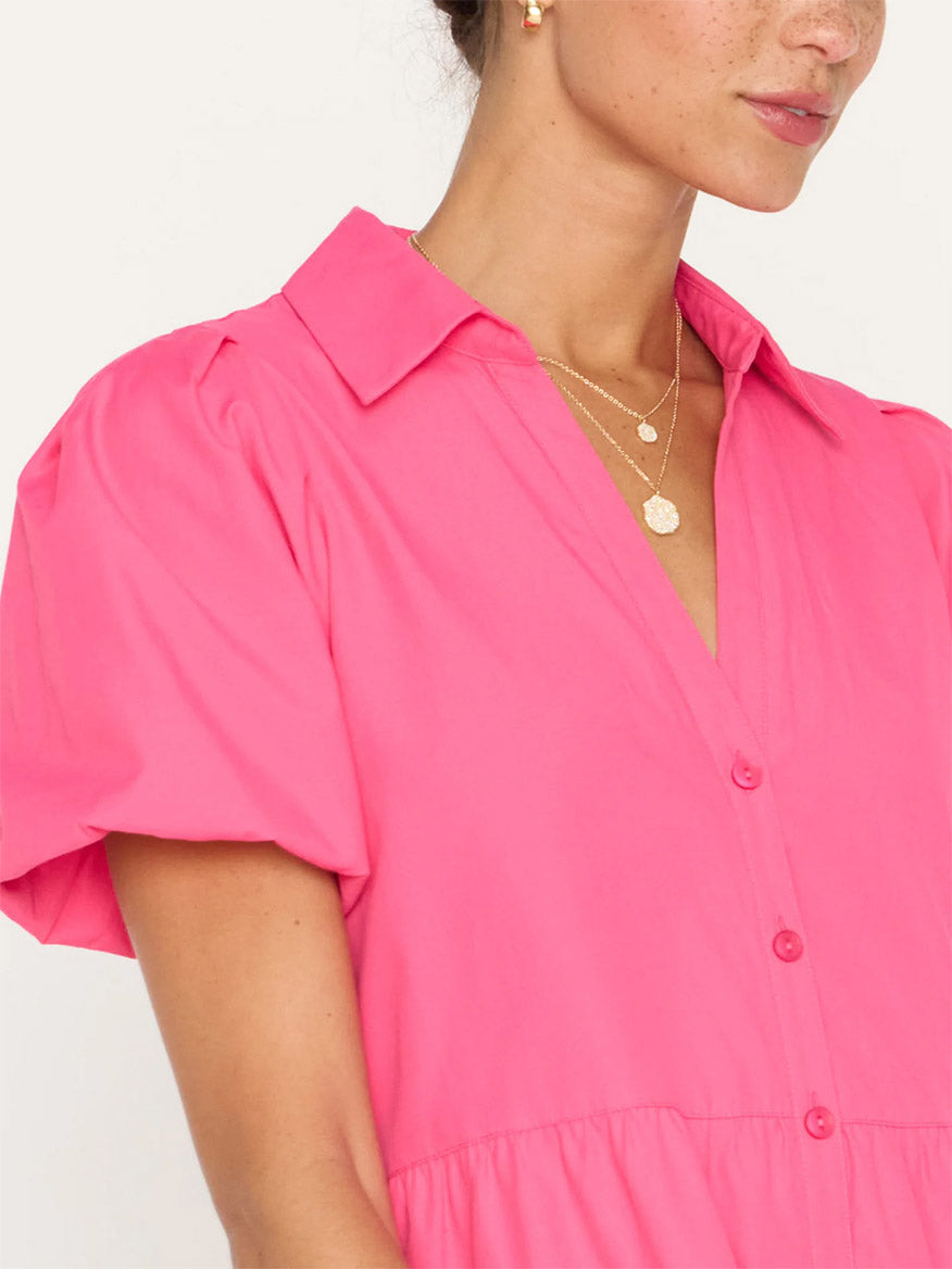 Close-up of a woman wearing a Brochu Walker Havana Mini Dress in Hot Pink with button details, featuring a subtle collar and pleated design, accessorized with a delicate gold necklace and a tiered skirt.
